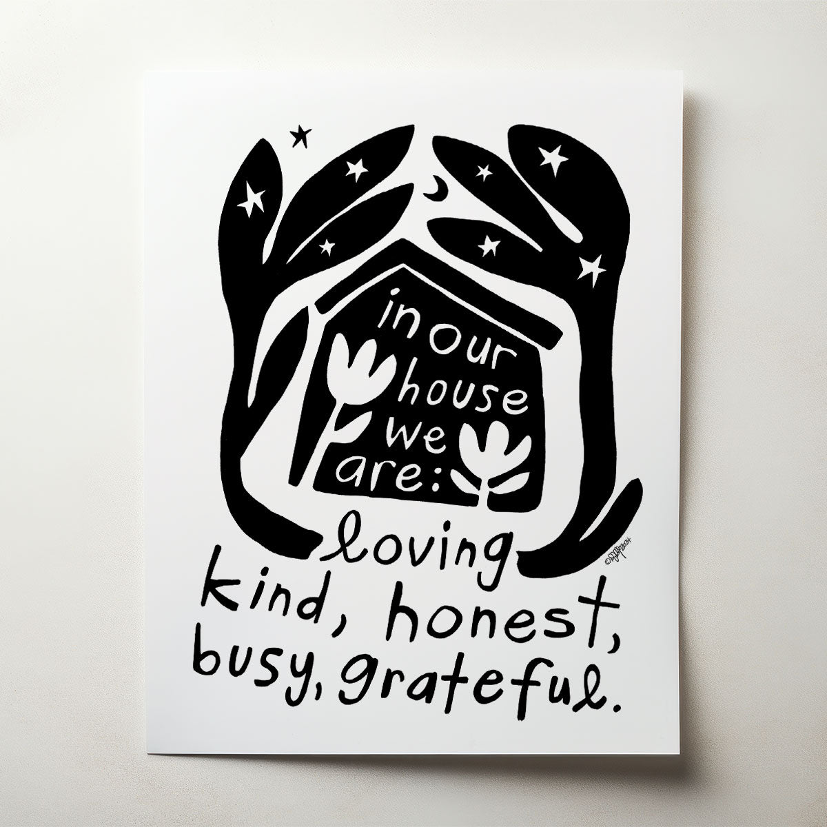 Decorative wall art with text 'in our house we are: loving, kind, honest, busy, grateful.' on paper.