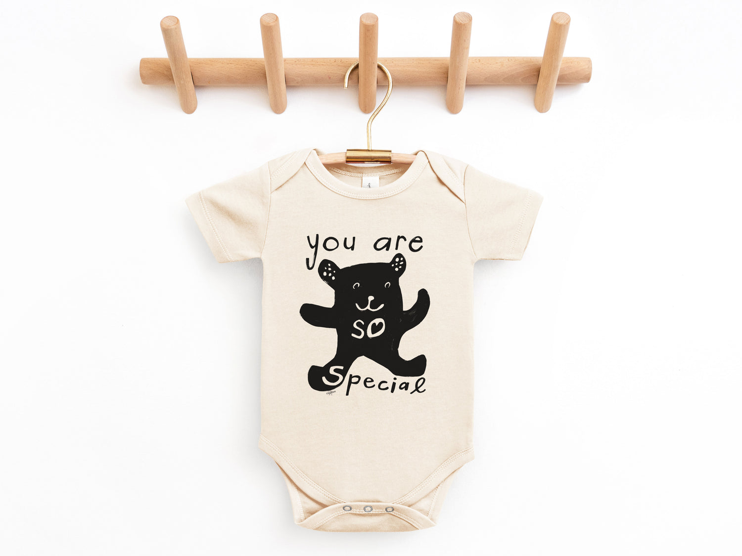 Baby onesie with bear graphic and text hanging on a wooden rack against a white background