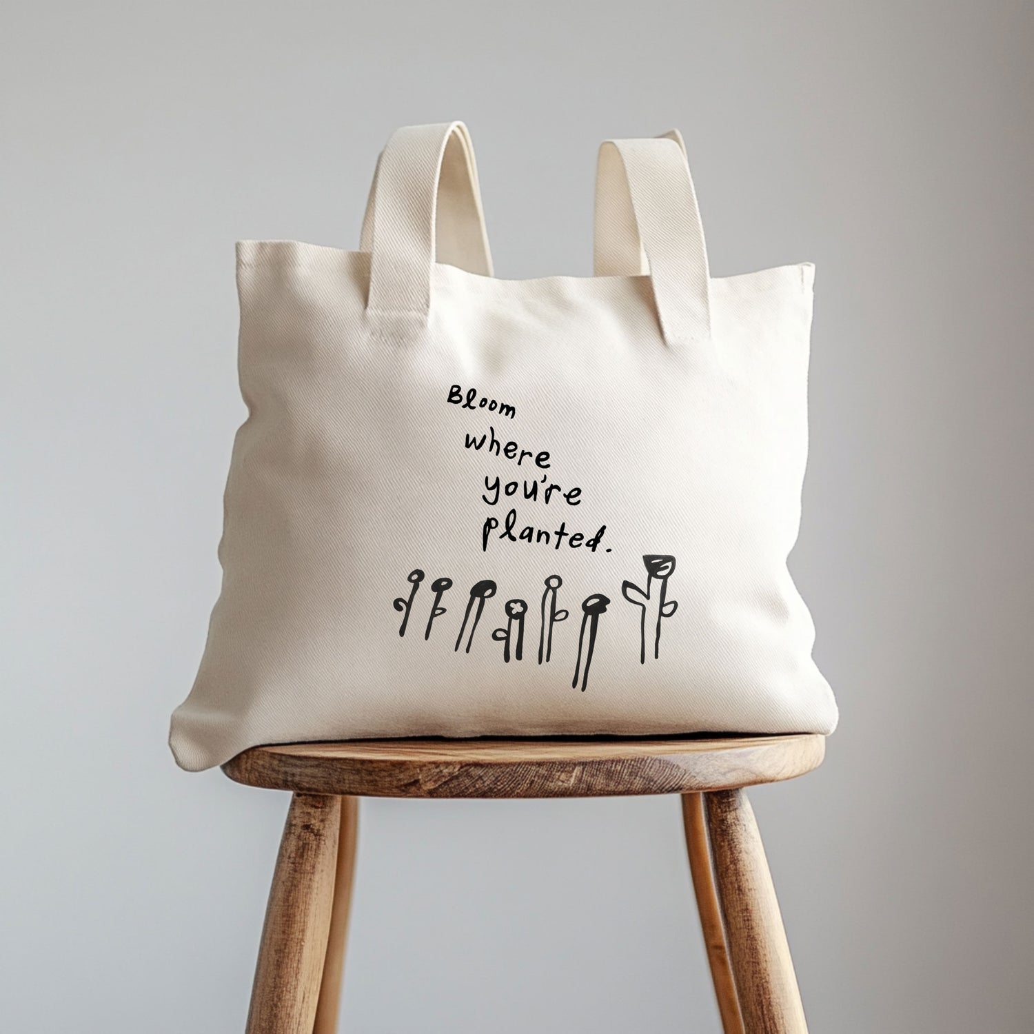 Beige tote bag with motivational quote on a wooden stool against a gray background