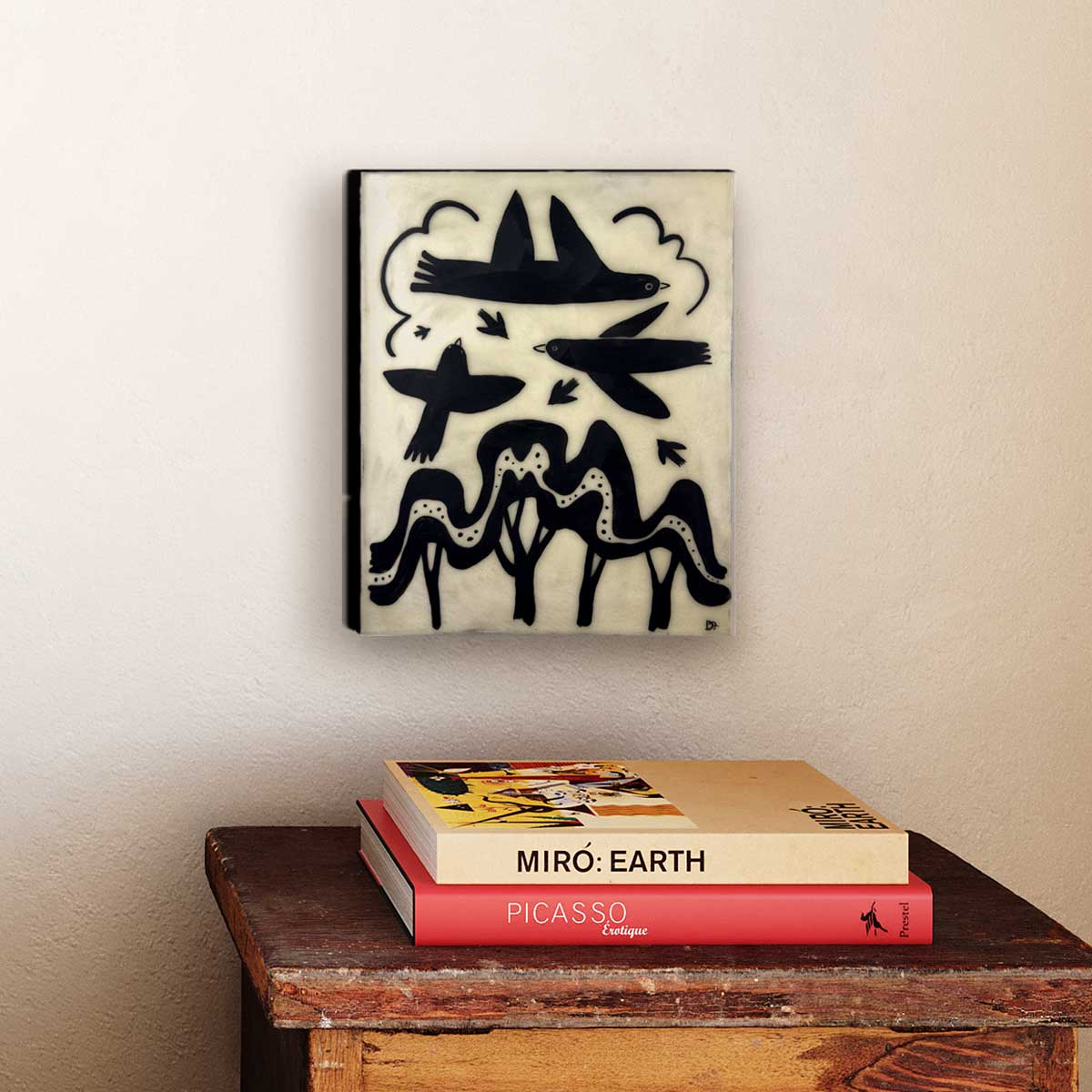 Unframed artwork of black abstract birds on a beige wall with books below.