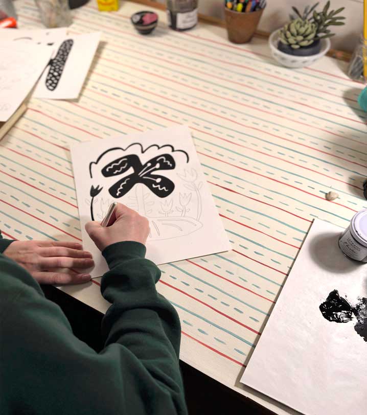 Artist painting on a piece of paper with on an art table with art supply items.